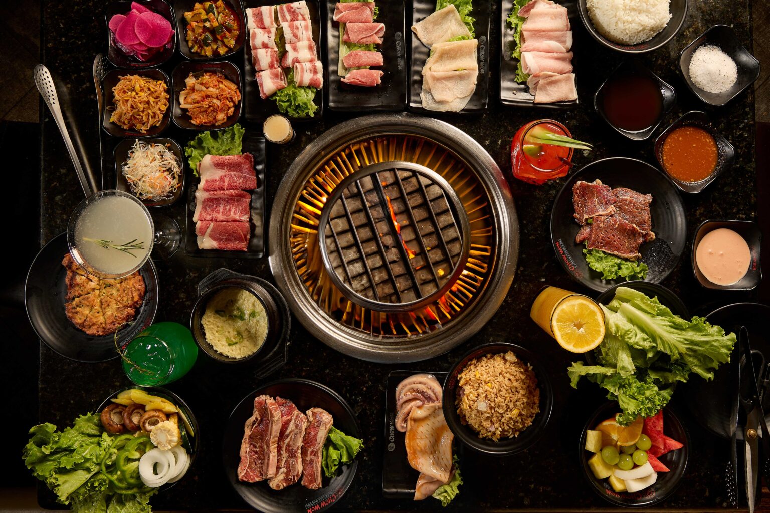 A full Chow One Korean BBQ spread: premium meats, banchan, and sides around the live tabletop grill